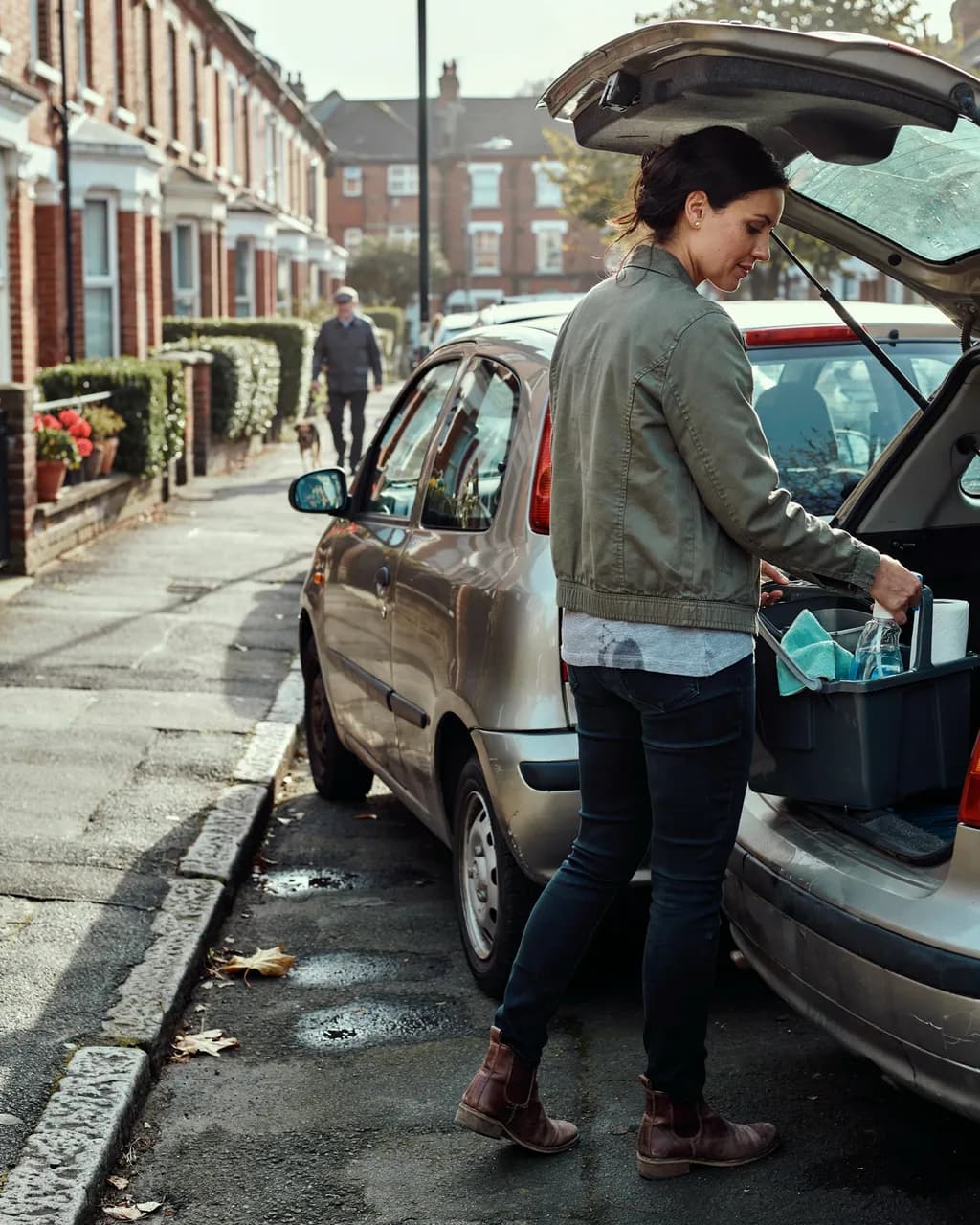An independent cleaner lifting a caddy of cleaning supplies out of a car boot on a terraced street