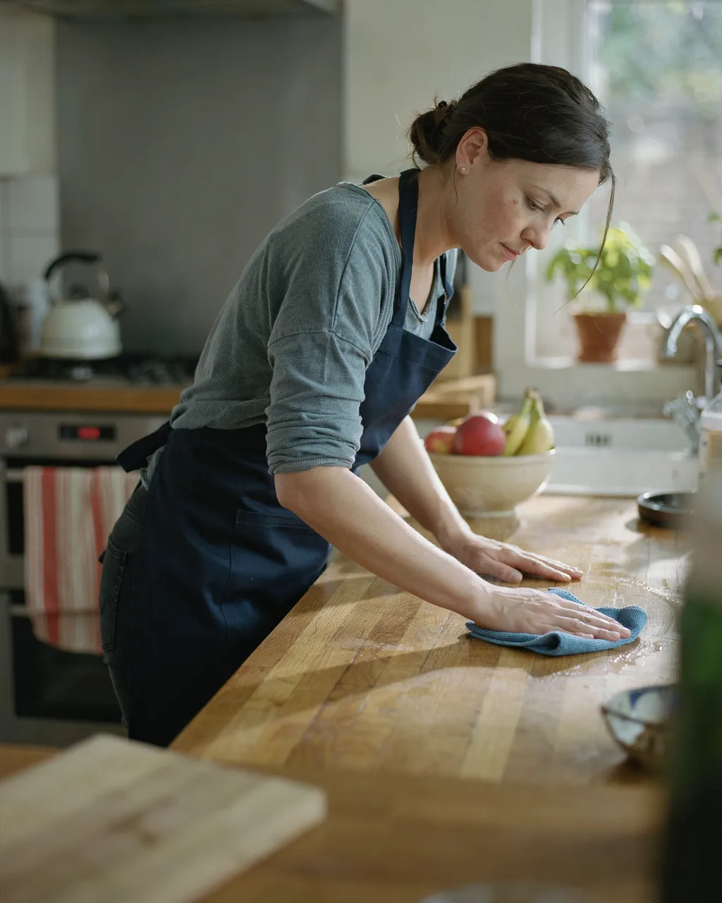 An independent cleaner wiping down a wooden kitchen worktop in natural light