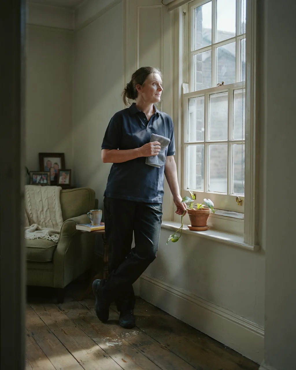 A cleaner pausing by a sash window in a customer's living room, holding a cloth